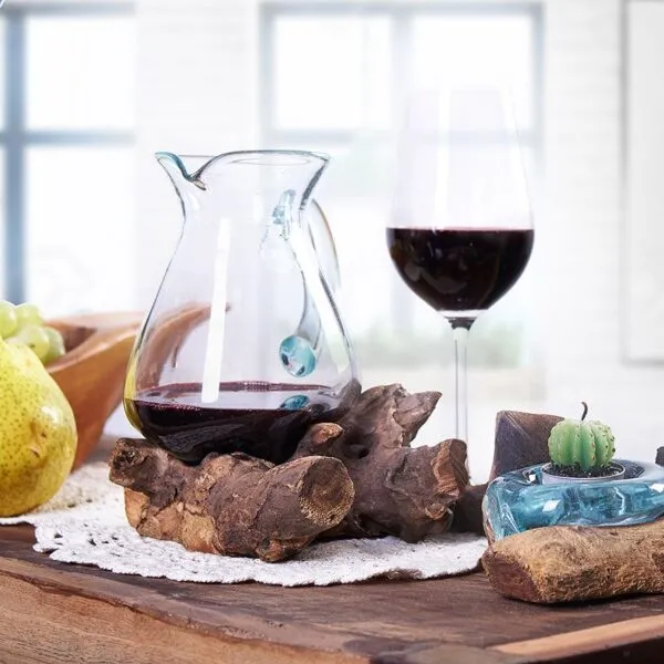 A rustic wine table with red wine decanter, glass, green grapes, pear, and cactus candle.