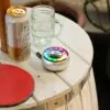 A rustic wooden table with beer can, glass mug, LED speaker, and red ping pong paddle.