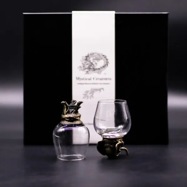 Two crystal glasses with bronze dragon bases in front of a black “Mystical Creatures” gift box.