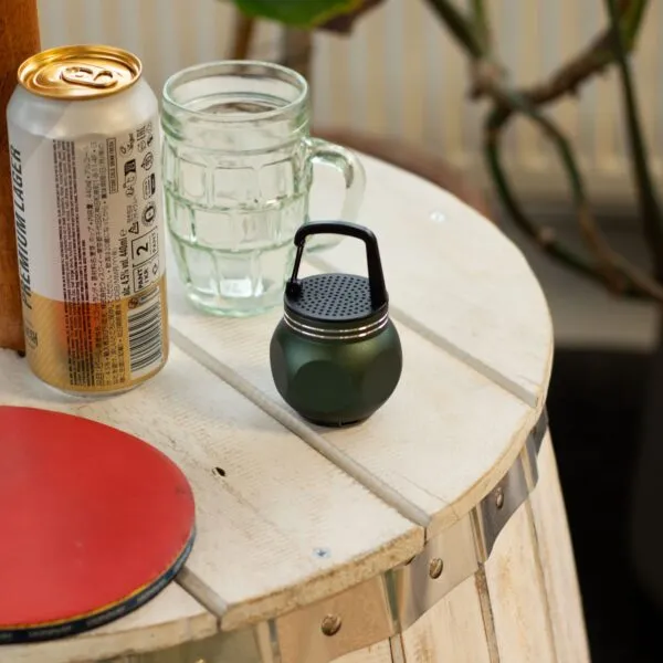 A rustic wooden table with a beer can, glass mug, green speaker, and red ping pong paddle.