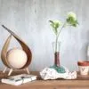 Minimalist wooden table with glass vase, green flowers, notebook, and natural decorative accents.