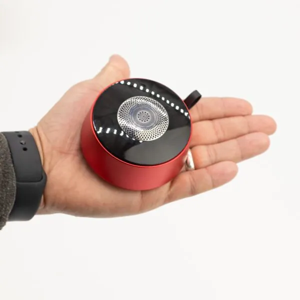A hand holding a small red and black portable speaker against a plain white background.