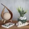 bG9jYWw6Ly9tZWRpYS8xUi80RS82MFIzMEMxRzZSVDM0RTFSLzYzYTM5YTI4LmpwZWc.webp Minimalist tabletop decor with wooden ornament, glass vase, green plant, and nature-inspired notebook.