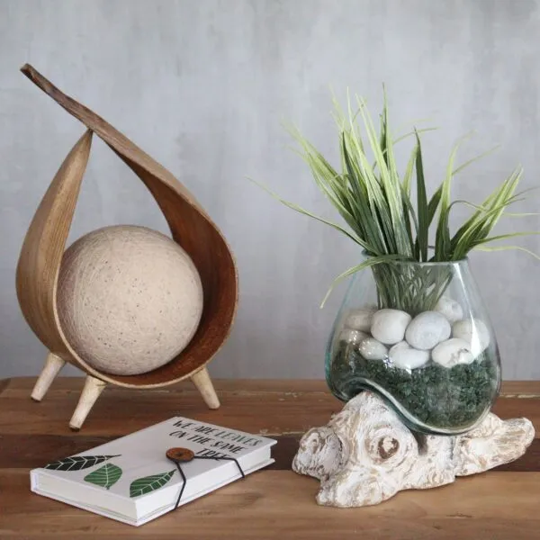 bG9jYWw6Ly9tZWRpYS8xUi80RS82MFIzMEMxRzZSVDM0RTFSLzYzYTM5YTI4LmpwZWc.webp Minimalist tabletop decor with wooden ornament, glass vase, green plant, and nature-inspired notebook.