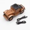 A vintage-style bronze and wood Bluetooth speaker shaped like a classic car with USB and aux cables.