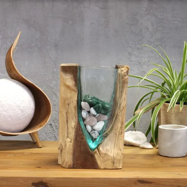 Rustic wooden and glass vase with gemstones on a wooden table beside plant and geode.