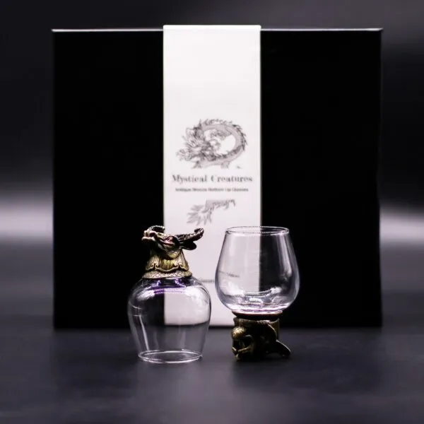 Two bronze-based dragon-themed glass cups in front of a black Mystical Creatures gift box.