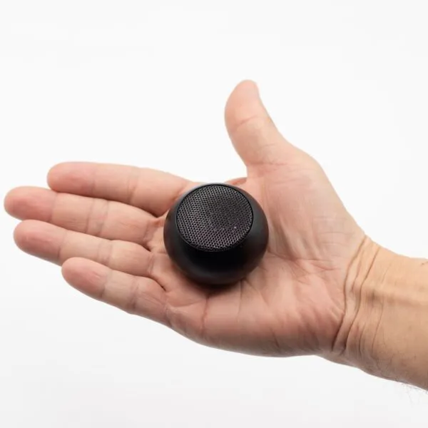 A person holding a small black portable speaker in their open hand against a white background.