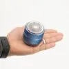 A hand holding a small metallic blue cylindrical electronic device against a white background.