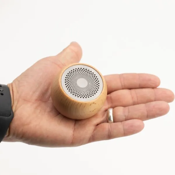 Stocking Filler A hand holding a small round wooden portable speaker with a metal grille on top.