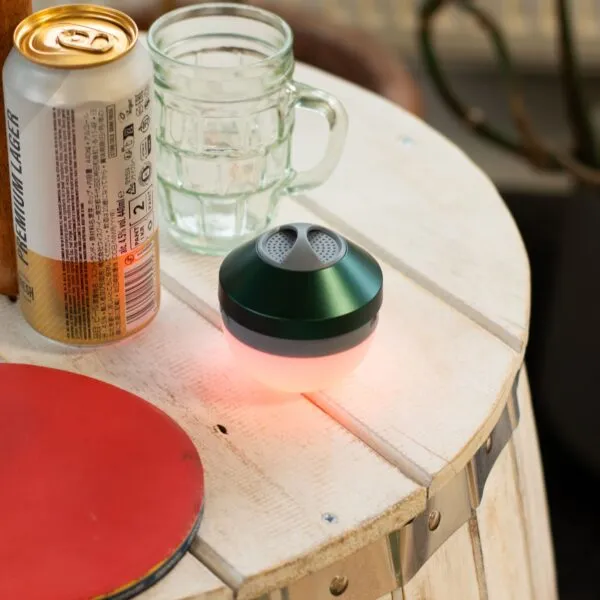A can of Japanese premium lager, empty glass mug, and glowing pink device on a wooden table.