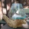Hand-blown turquoise glass bowl resting on natural driftwood base outdoors in sunlight.