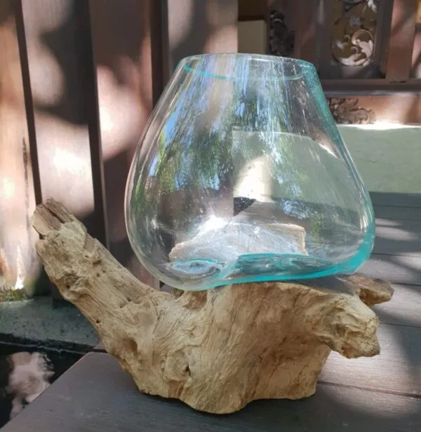 Hand-blown turquoise glass bowl resting on natural driftwood base outdoors in sunlight.