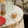 A small wooden table with a Bluetooth speaker, glass mug, drink can, and red ping-pong paddle.