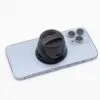 Silver iPhone with triple cameras and black collapsible grip lying on a white surface.