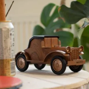 Retro wooden vintage car Bluetooth speaker on light wood surface with leafy plant background.