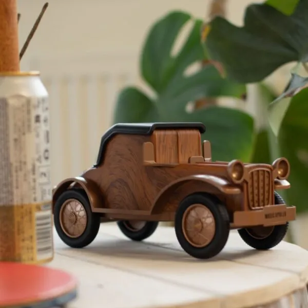 Retro wooden vintage car Bluetooth speaker on light wood surface with leafy plant background.