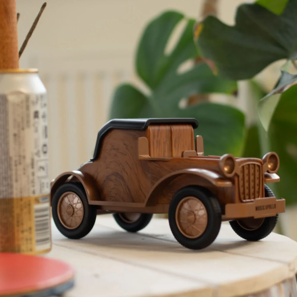 Retro wooden vintage car Bluetooth speaker on light wood surface with leafy plant background.