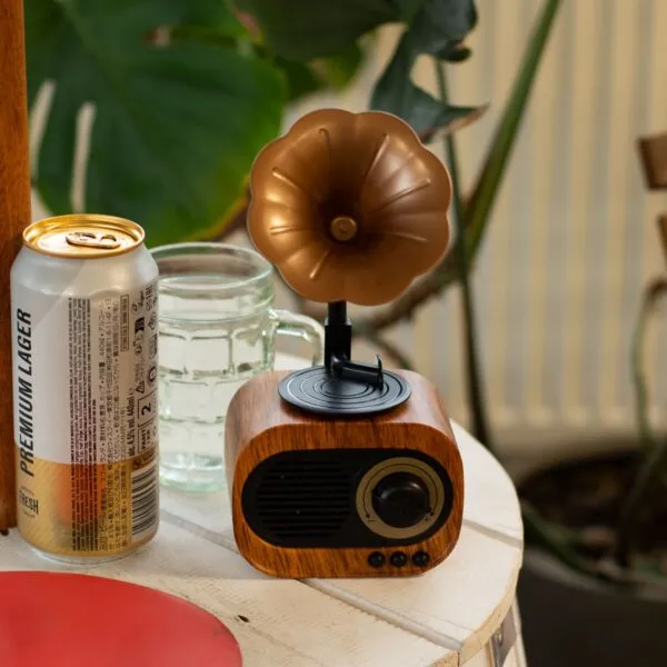 Vintage wooden Bluetooth gramophone speaker with gold horn beside a cold beer can and glass.