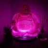 Best Housewarming Gifts With Personality. Colourful home decor trends. A glowing magenta laughing Buddha statue beside a small succulent and reed diffuser.