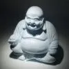A pale blue crackle-glazed Laughing Buddha statue seated and smiling joyfully against a dark background.