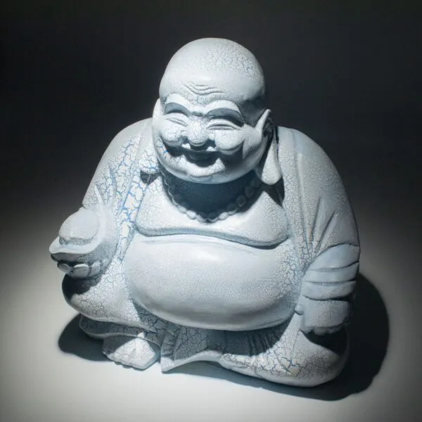 A pale blue crackle-glazed Laughing Buddha statue seated and smiling joyfully against a dark background.