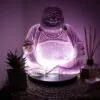 A glowing purple Laughing Buddha lamp beside a succulent plant and patchouli reed diffuser.