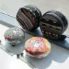 Two colourful mini steel tongue drums with matching fabric cases and mallets beside a window.