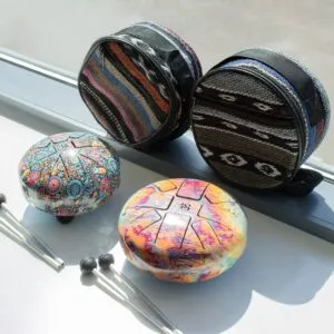 Two colourful mini steel tongue drums with matching fabric cases and mallets beside a window.