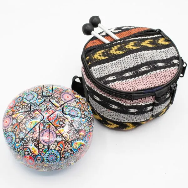 A patterned steel tongue drum and bohemian carrying bag with mallets on a white background.