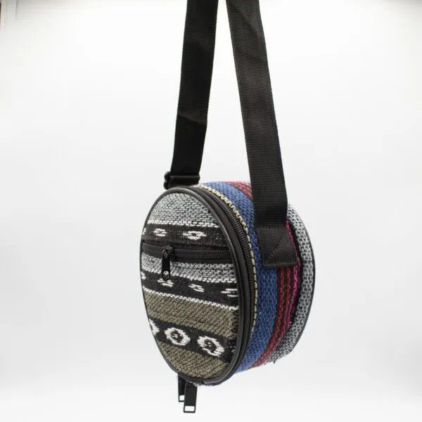 Small circular woven bag with colourful geometric patterns hanging against a white background.