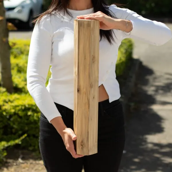 Woman holding a natural tan wooden healing rain stick outdoors.