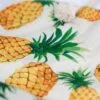 Textured beige burlap fabric featuring a tropical pineapple print and decorative cotton tassel.