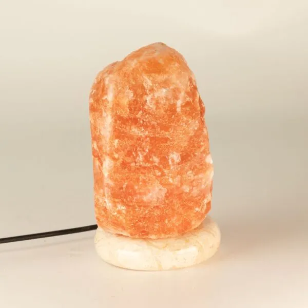 Raw pink Himalayan salt lamp mounted on a polished white marble base.