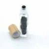 Clear glass roller bottle filled with black gemstone chips beside a natural wooden cap.