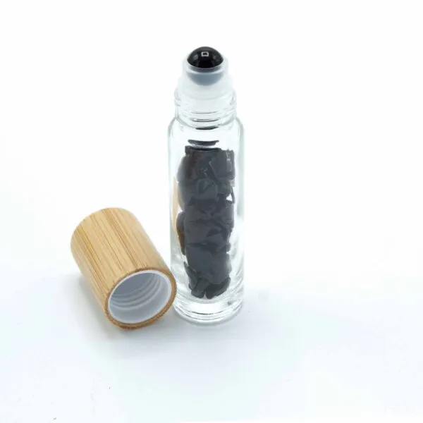 Clear glass roller bottle filled with black gemstone chips beside a natural wooden cap.