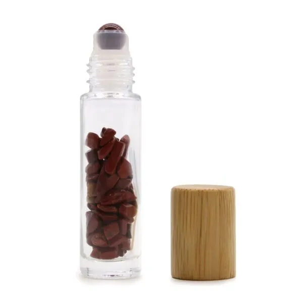 Clear glass roller bottle filled with red jasper chips beside a natural bamboo cap.