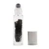 Clear glass essential oil roller bottle filled with black crystals beside a silver cap.