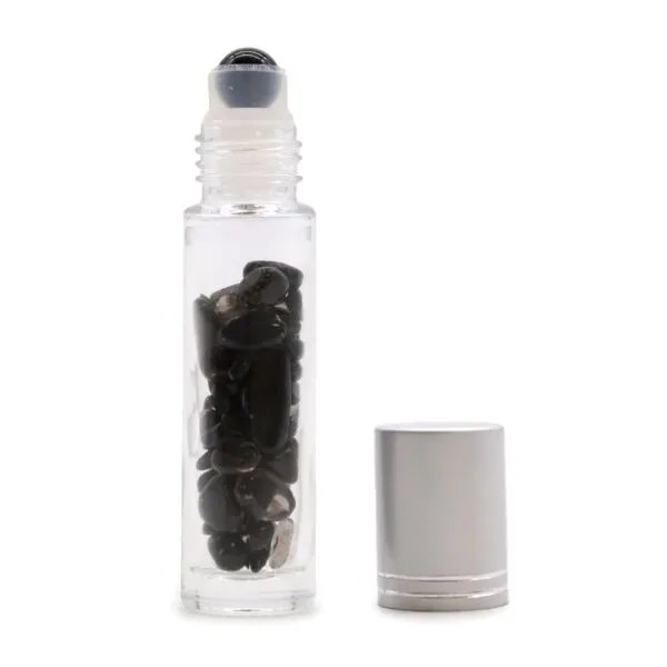 Clear glass essential oil roller bottle filled with black crystals beside a silver cap.