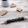 Crystal Healing Wand Etched Wood Black Pink Dual Gem Ends Etched black crystal healing wand with dual pink stone ends on grey wood.