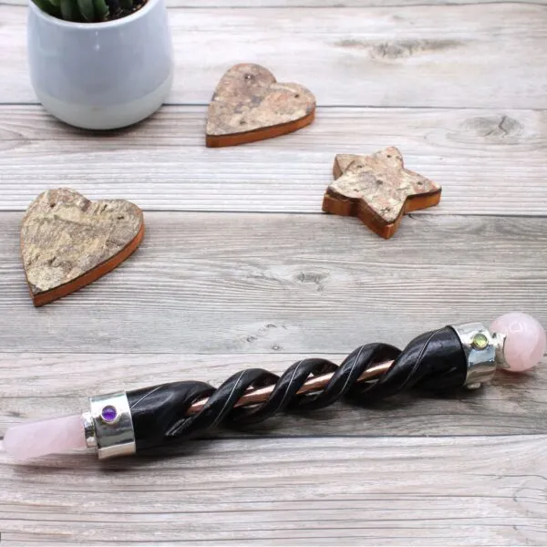 Crystal Healing Wand Etched Wood Black Pink Dual Gem Ends Etched black crystal healing wand with dual pink stone ends on grey wood.