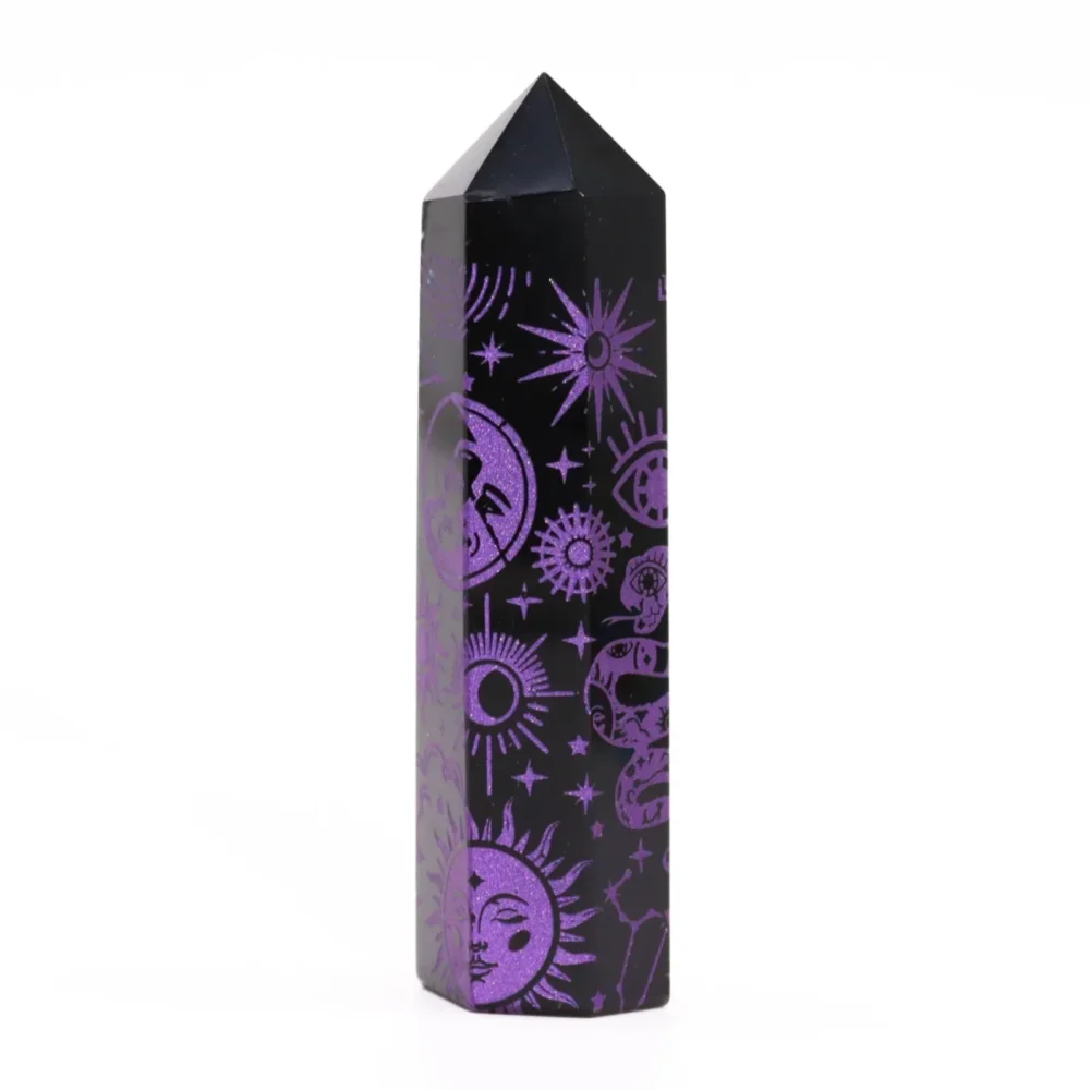 Six-sided black stone obelisk point carved with sparkly purple celestial symbols.