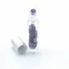 Clear glass essential oil roller bottle with purple gemstones and an open silver cap.