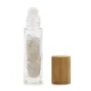 Clear quartz glass essential oil roller bottle filled with crystals beside a bamboo cap.