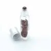 Clear glass roll-on vial with reddish-brown gemstones next to a matte silver cap.