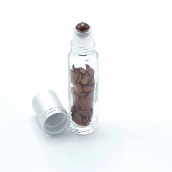 Clear glass roll-on vial with reddish-brown gemstones next to a matte silver cap.