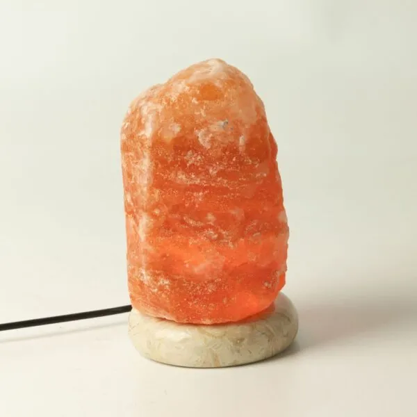 Glowing orange Himalayan salt lamp on a natural stone base with USB cable.