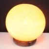 Sphere Salt Lamp Himalayan Crystal Golden Dark Wooden Base Glowing golden Himalayan salt lamp sphere emitting warm light on a dark wooden base.