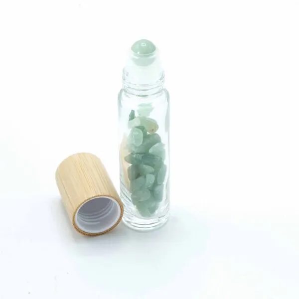 Glass roller bottle filled with green aventurine crystals beside a bamboo cap.