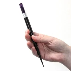 A hand holding a dark purple amethyst crystal healing wand with a wooden handle.